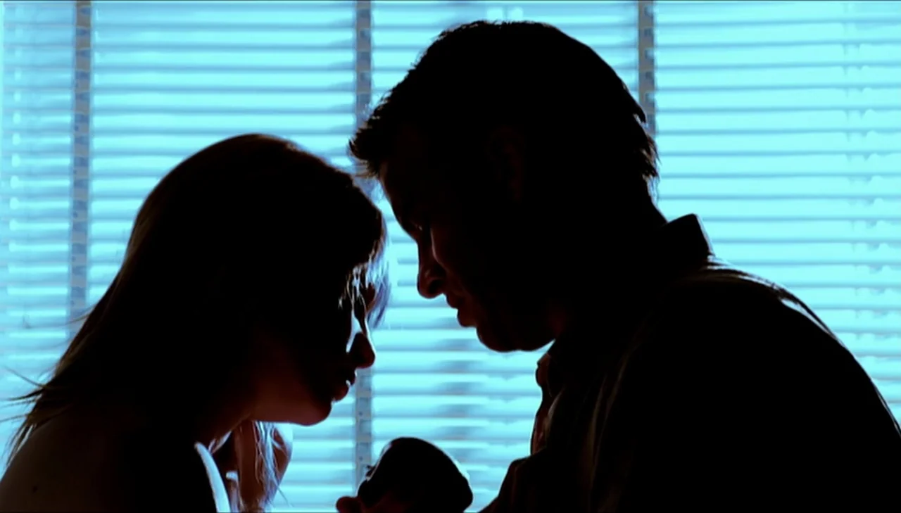 Dark Country (2009) movie still: medium — An interior space is illuminated by daylight filtering through closed horizontal window blinds. A man and…