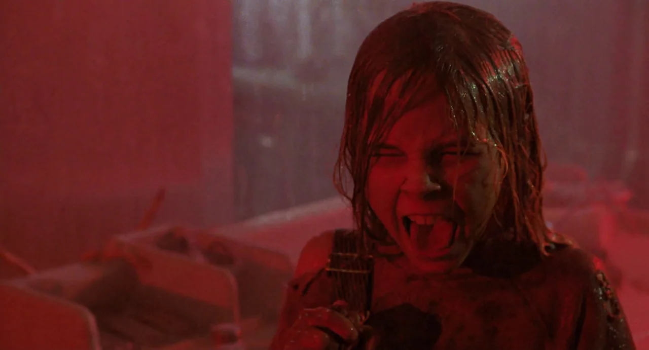 Aliens (1986) movie still: closeup — A dark bathroom interior is flooded with intense, artificial red light. A young girl with wet hair screams…