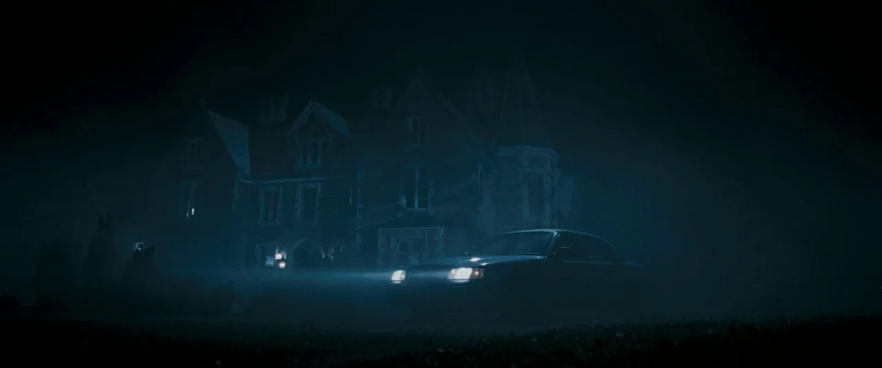 Dead Silence (2007) movie still: wide — A large multi-story mansion stands in the darkness shrouded by thick ground fog. A sedan with its headlights…
