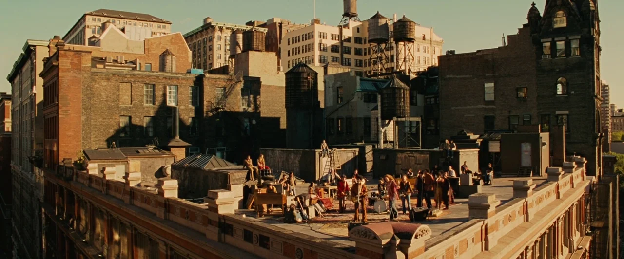 Across the Universe (2007) movie still: establishing — An urban rooftop features a collection of people gathered around musical equipment and…