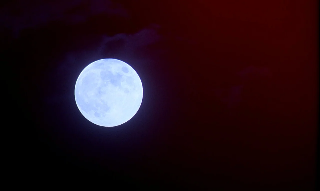 Dellamorte Dellamore (1994) movie still: establishing — A full moon illuminates the center of a pitch-black and deep red night sky. Dark, wispy…