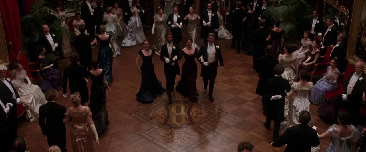 The Age of Innocence (1993) movie still: wide — A spacious, wood-paneled ballroom features a central inlaid floor medallion and surrounding guests.…