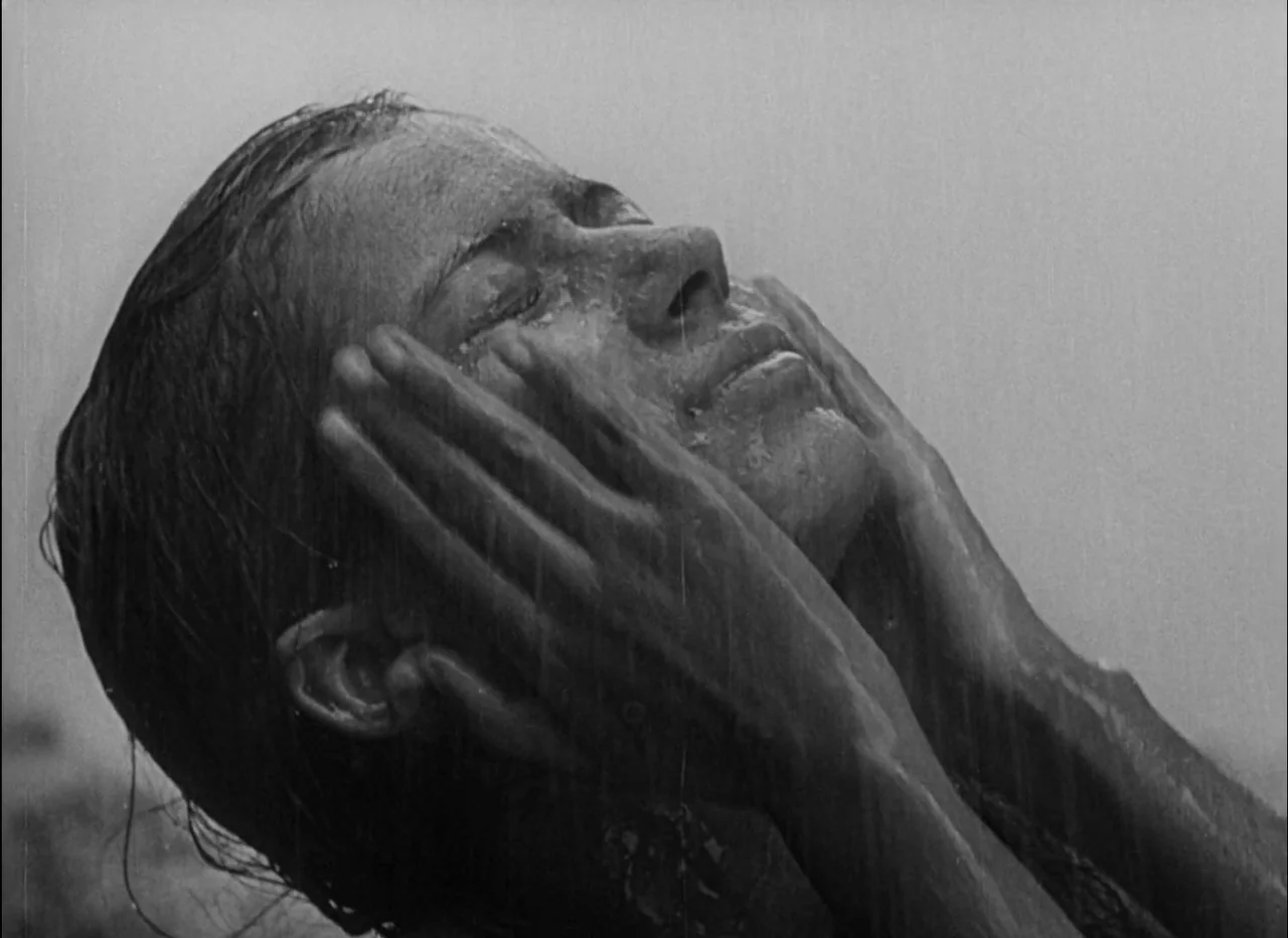 Pather Panchali (1955) movie still: closeup — An individual stands in the open air while rain falls over their face. The person rests both hands…