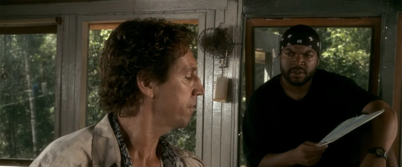 Anaconda (1997) movie still: medium — A rustic wooden shack with large framed windows overlooks a dense forest exterior. Two men stand inside…