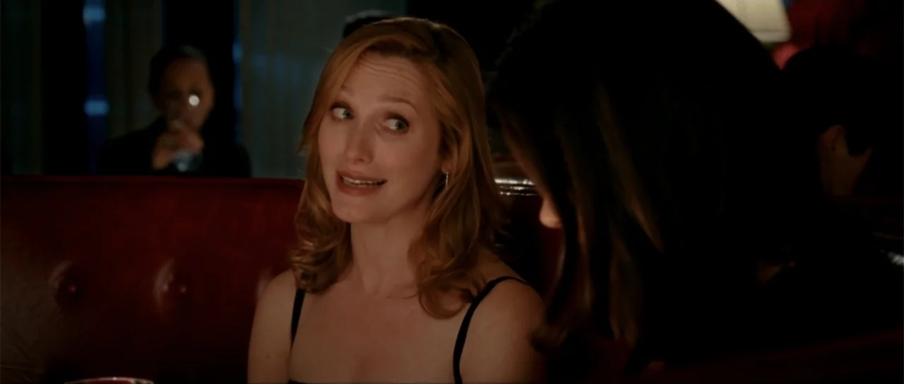 The Rebound (2009) movie still: medium — A dark booth with deep red upholstered seating inside a restaurant or bar. A blonde woman in a black top…