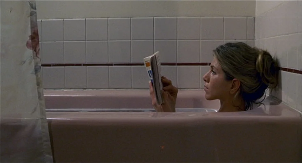 The Good Girl (2002) movie still: medium — A vintage-style bathroom features a pink enamel tub against white subway tile walls. A woman with hair in…