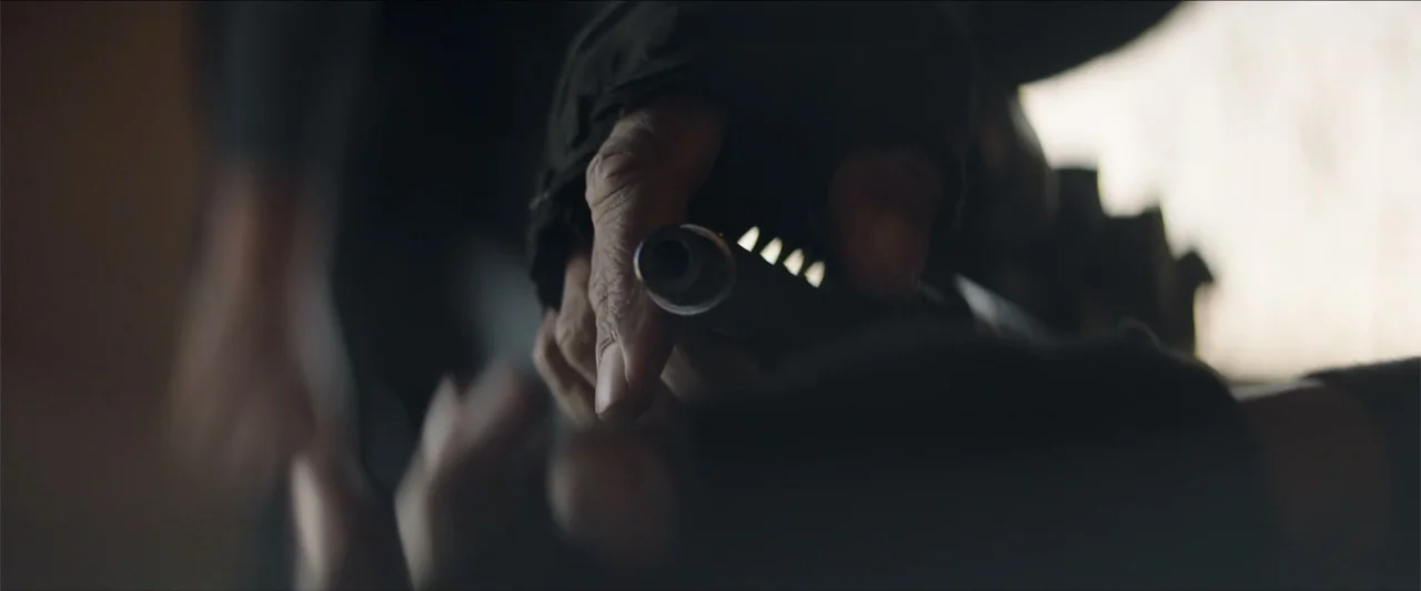 Redemption Day (2021) movie still: closeup — A dimly lit interior shows a close-up of a person gripping a firearm. The focus is on the textured skin…