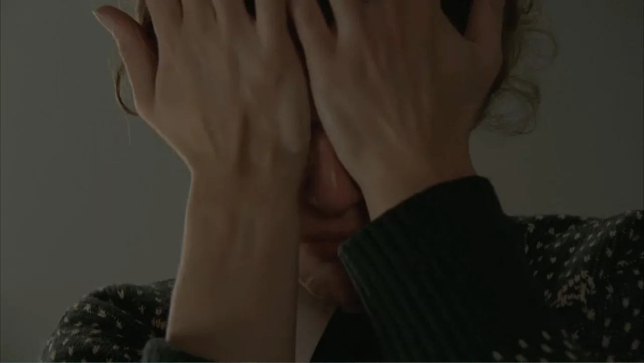 Temple Grandin (2010) movie still: closeup — A dimly lit, featureless indoor space serves as the background. A woman holds her hands over her face…