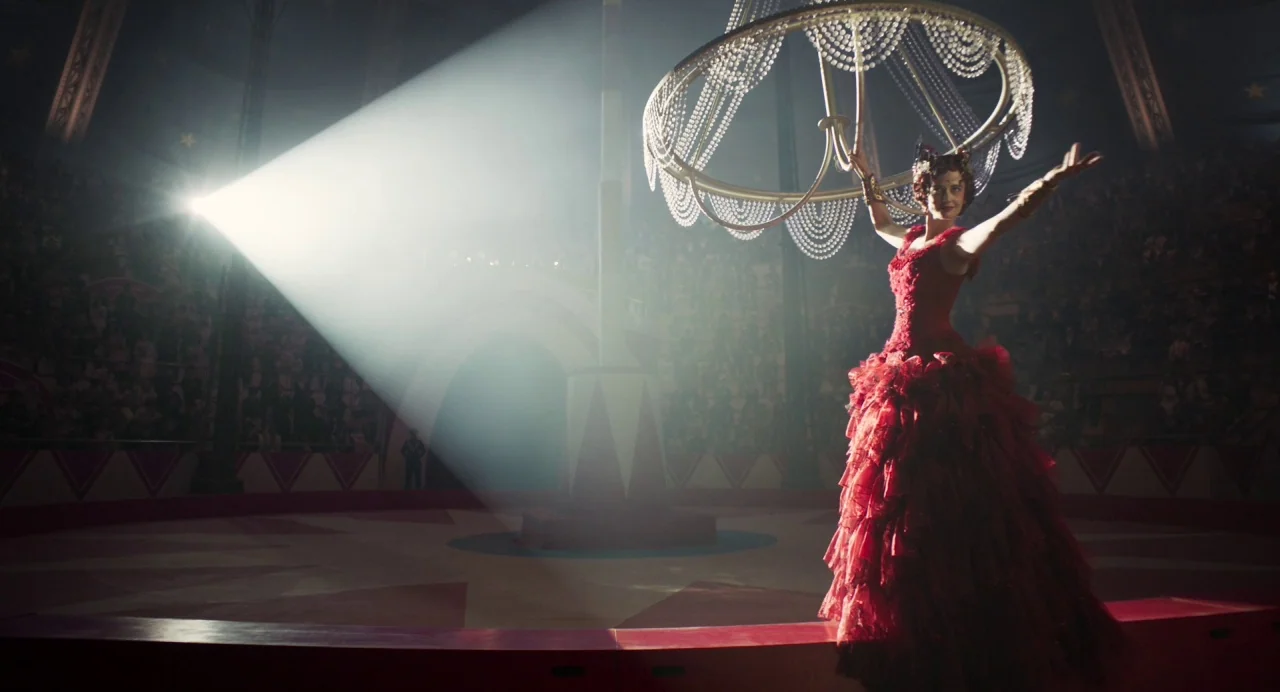 Dumbo (2019) movie still: fullbody — A large circus tent interior features a central performance ring and bleachers in darkness. A woman in a red…