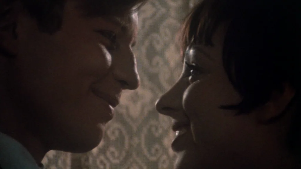 Cabaret (1972) movie still: closeup — Two individuals stand closely together against a textured wall with subtle pattern work. The pair look…