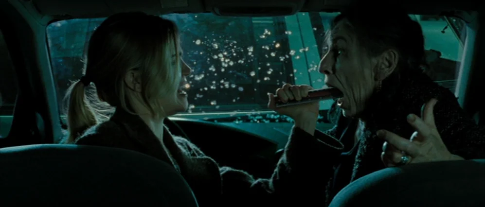 Drag Me to Hell (2009) movie still: medium — The interior of a car at night with teal-tinted lighting. An older woman holds a metal rod against the…