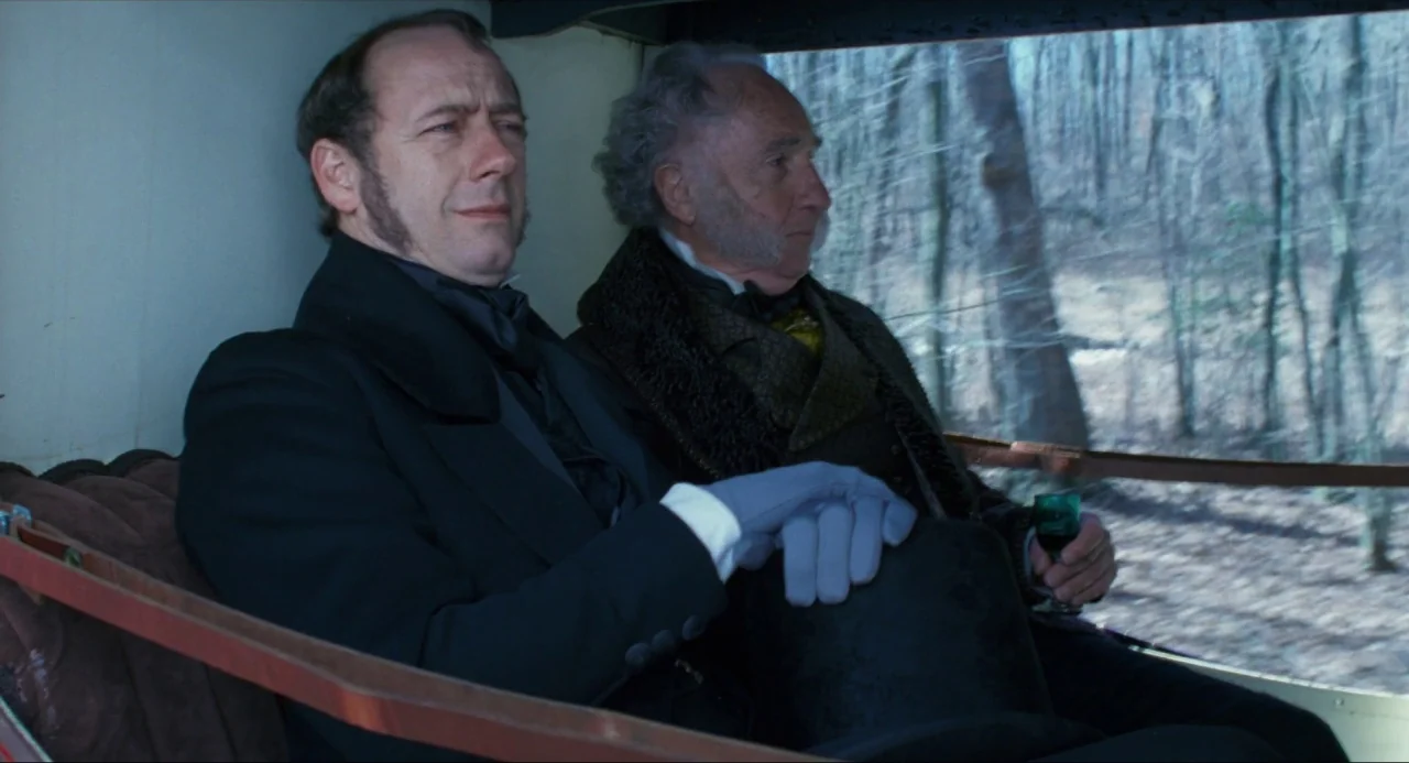 Amistad (1997) movie still: medium — The interior of a 19th-century carriage with brown upholstered seating and window view. Two formally dressed…