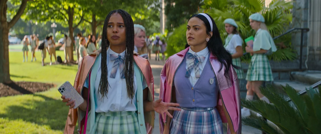 Do Revenge (2022) movie still: medium — A grassy school campus with paved pathways lined by trees and lush greenery. Two teenage girls in preppy…