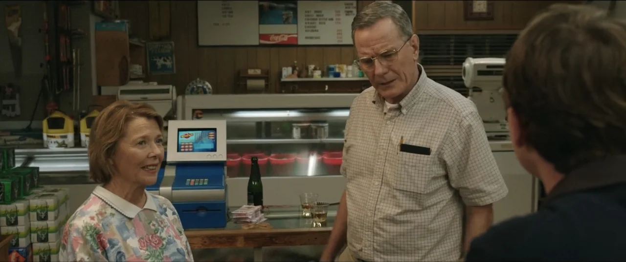 Jerry & Marge Go Large (2022) movie still: medium — A cluttered convenience store interior features a checkout counter with merchandise and a menu…