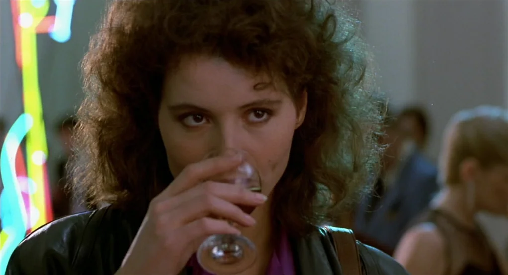 The Fly (1986) movie still: closeup — A dimly lit indoor space features colorful out-of-focus neon lights in the background. A woman in a leather…