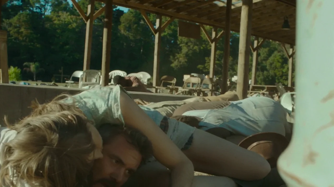 The Sacrament (2013) movie still: medium — An open wooden pavilion provides shade over a ground area in an outdoor setting. A young woman and a man…