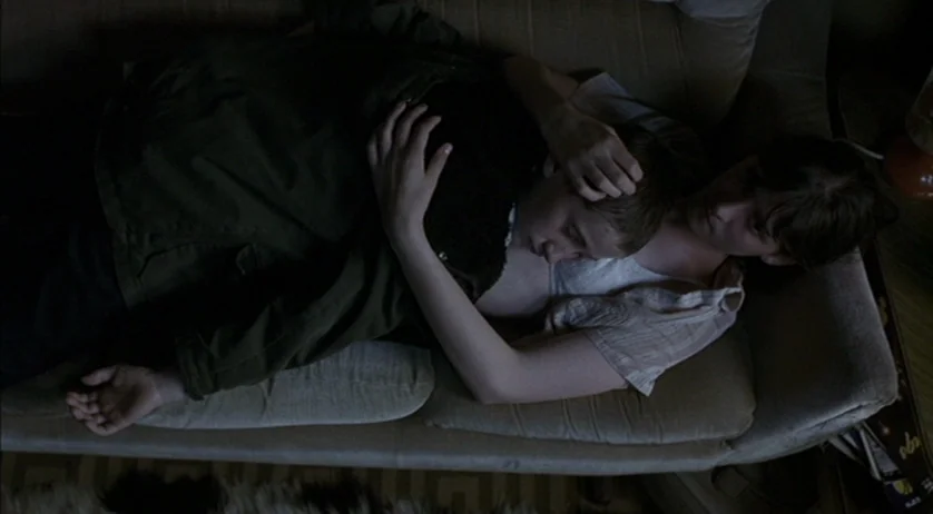 Ratcatcher (1999) movie still: medium — A dimly lit room features two people reclining together on a fabric sofa. They are resting their bodies…
