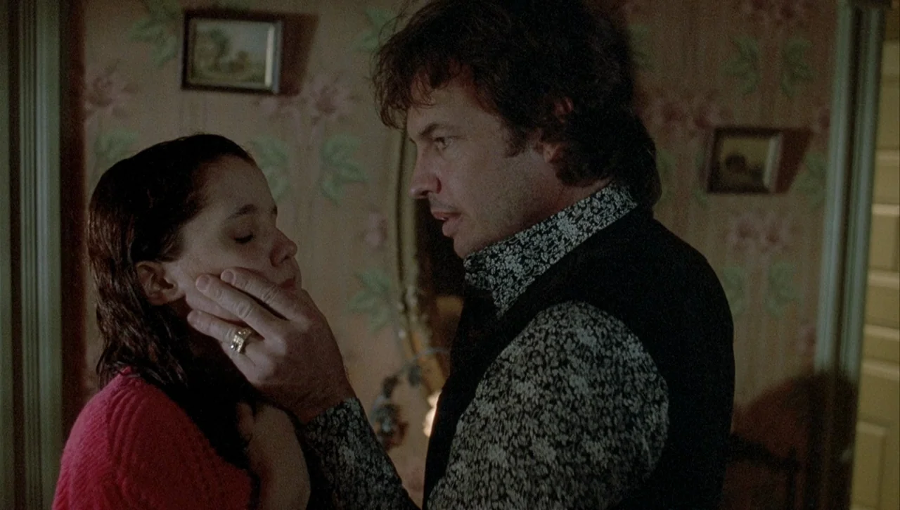 Necronomicon: Book of Dead (1993) movie still: medium — A dimly lit room with vintage patterned wallpaper features two framed pictures on the wall.…