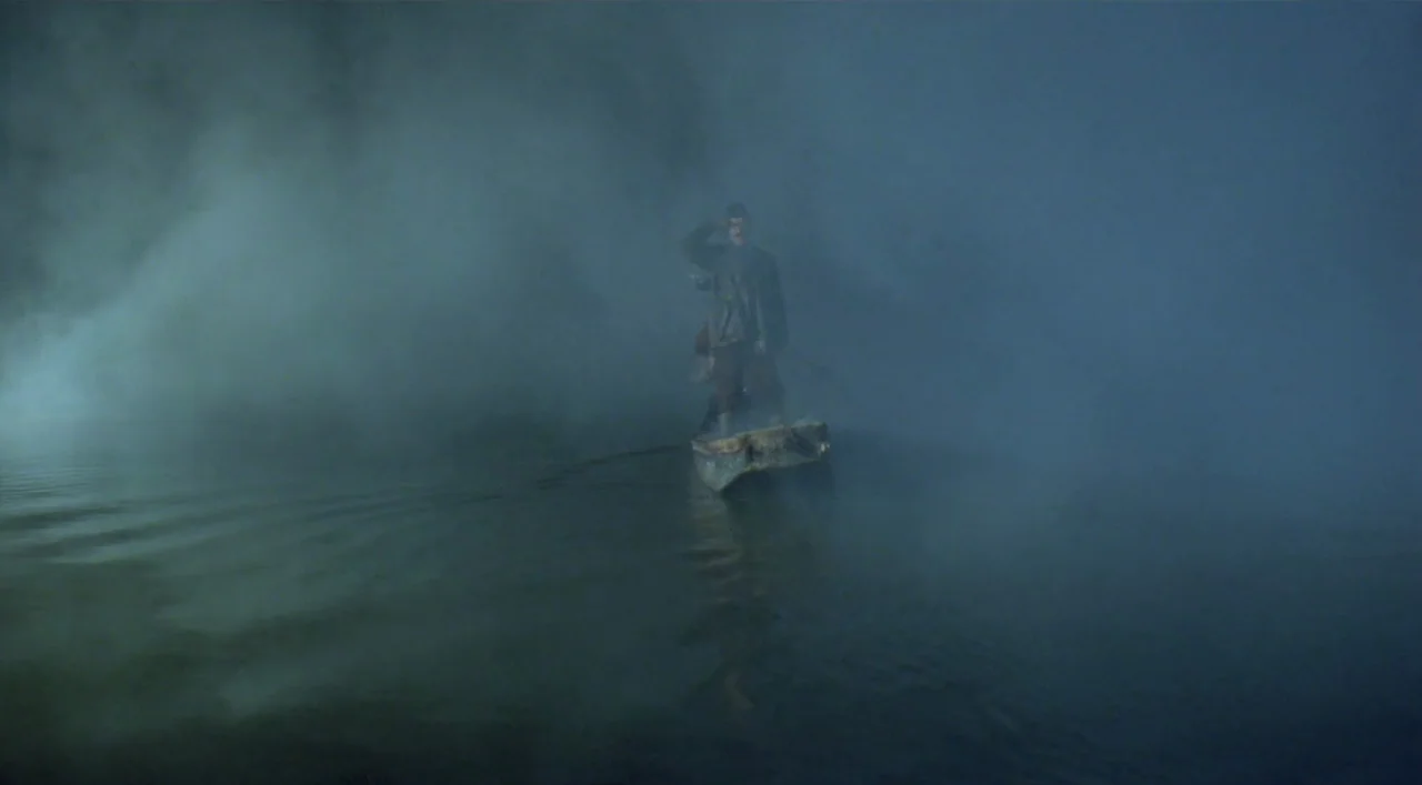 Underground (1995) movie still: wide — A man stands on a small, narrow boat navigating a dark river at night. Thick, low-hanging fog surrounds the…