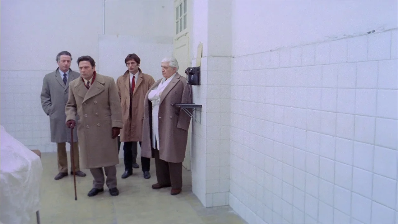 Death Occurred Last Night (1970) movie still: fullbody — A clinical hallway features sterile white tiled walls and a wall-mounted vintage telephone.…