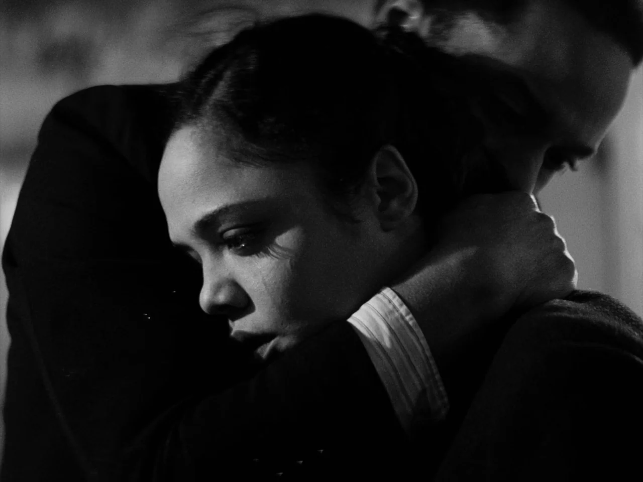 Passing (2021) movie still: closeup — A dark indoor space with minimal detail visible in the shadows. A man and a woman embrace closely in a dimly…