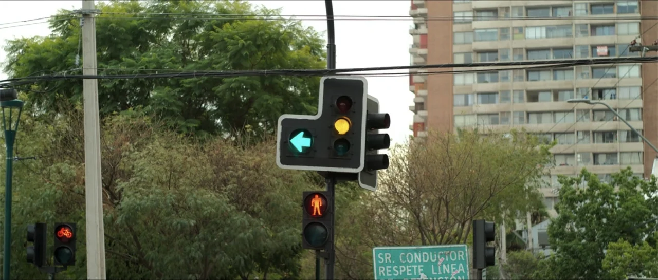 Disconnected 2 (2025) movie still: medium — An urban traffic signal stands prominently against a backdrop of trees and an apartment building. The…