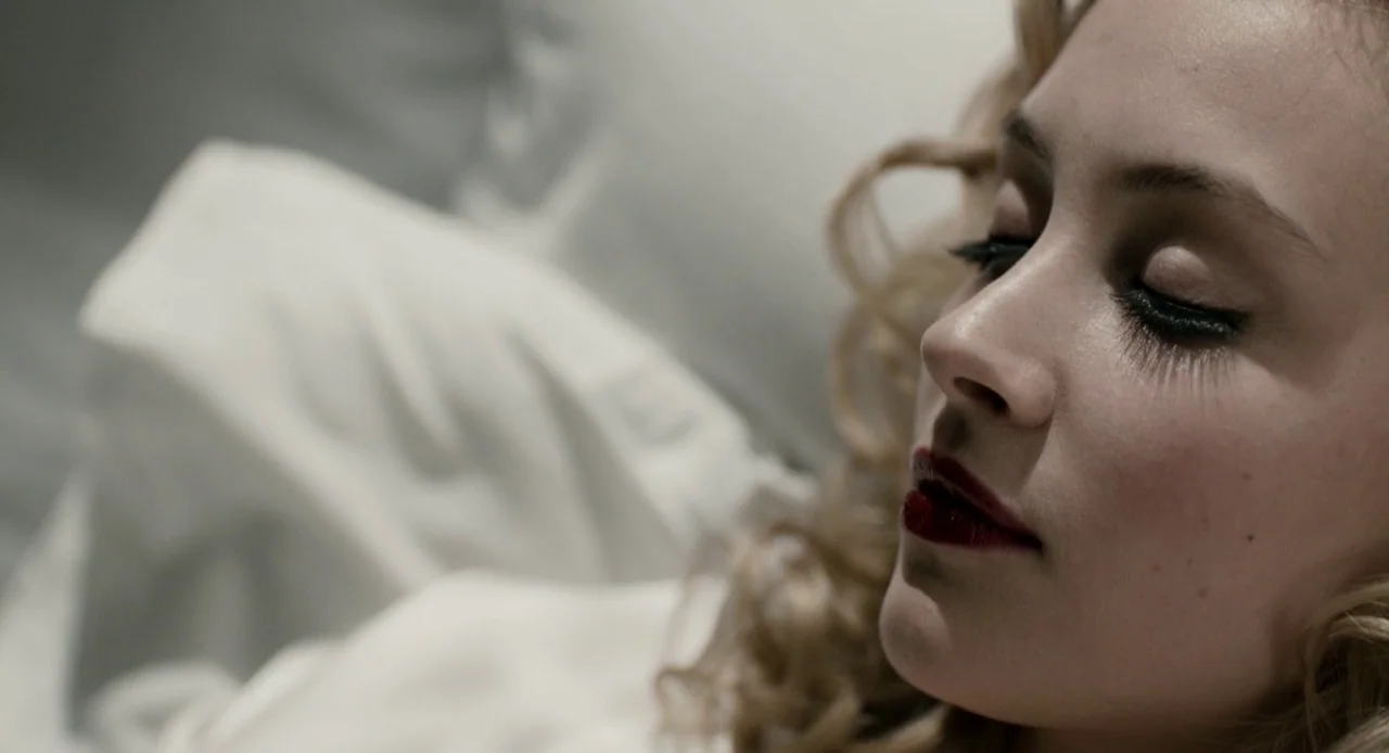 Antiviral (2012) movie still: closeup — A close-up of a person resting against soft, white fabric. The subject lies still with her eyes closed and…