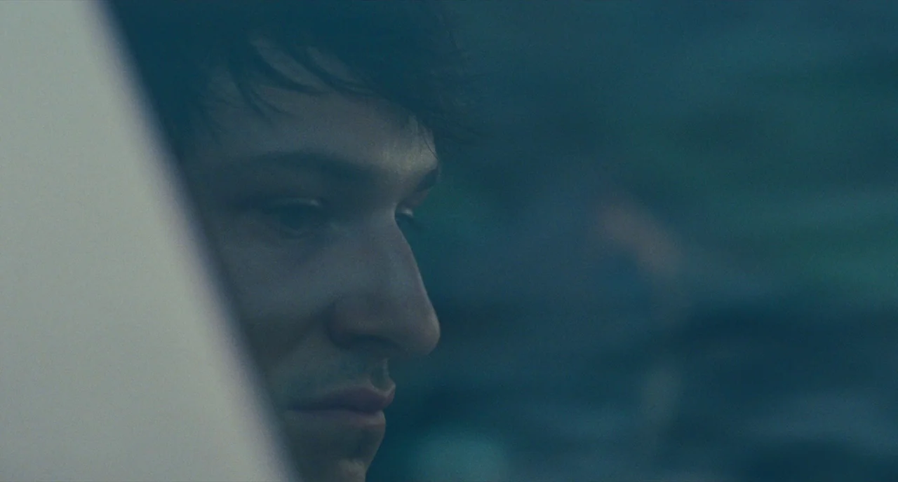 It’s Only The End Of The World (2016) movie still: closeup — A close-up shows a man viewed through a reflective train window at night. Blue-toned…
