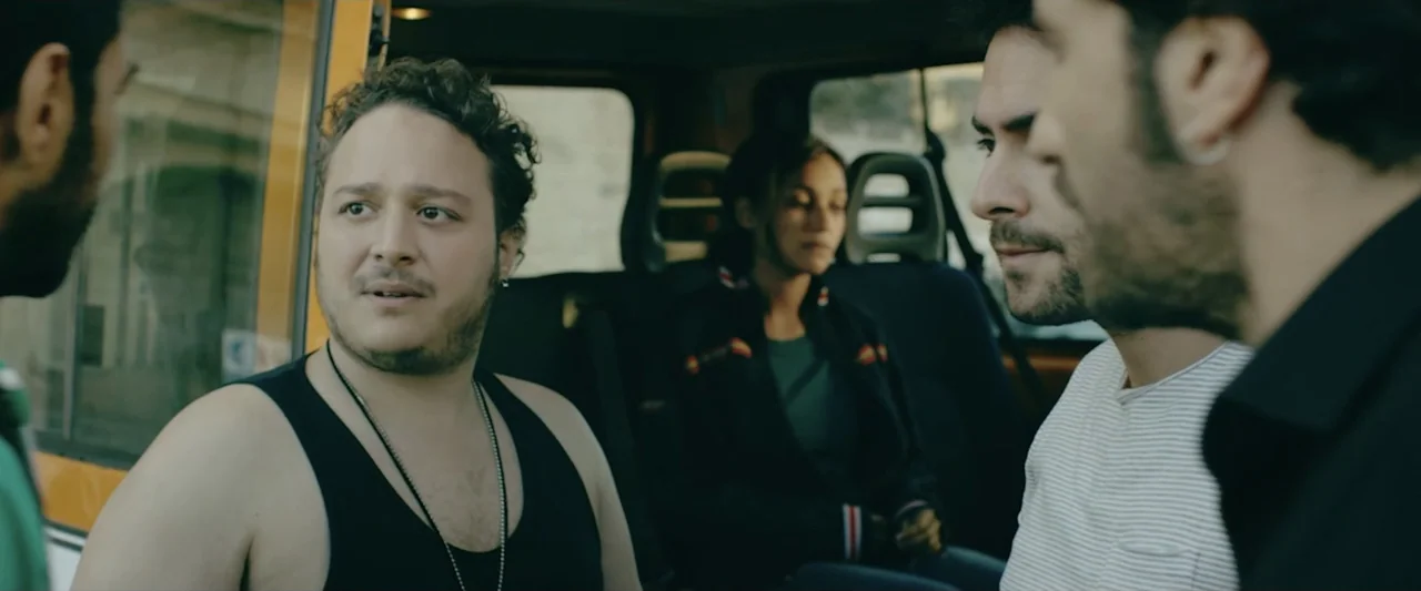 Taranta On the Road (2017) movie still: medium — A group of people sit inside the back of a van during the day. The occupants talk while looking…