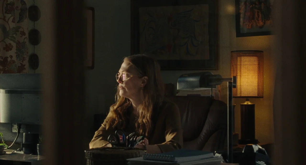 When You Finish Saving The World (2022) movie still: medium — A dimly lit home office features a leather chair and a warm desk lamp. A woman sits at…