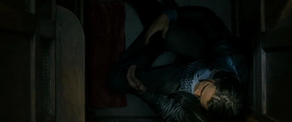 Ondine (2009) movie still: medium — A confined dark stall features a narrow red mat on the floor. A man in a dark jacket is lying on the floor in a…