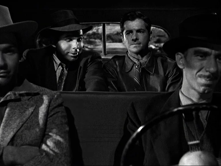 Saboteur (1942) movie still: medium — Four men sit closely together inside the cabin of a vintage automobile. They face forward and sideways,…