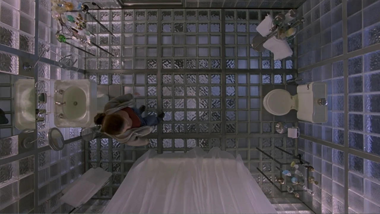 13 Ghosts (1960) movie still: fullbody — A minimalist bathroom features floor-to-ceiling glass block walls and a metal grid floor. A woman stands in…