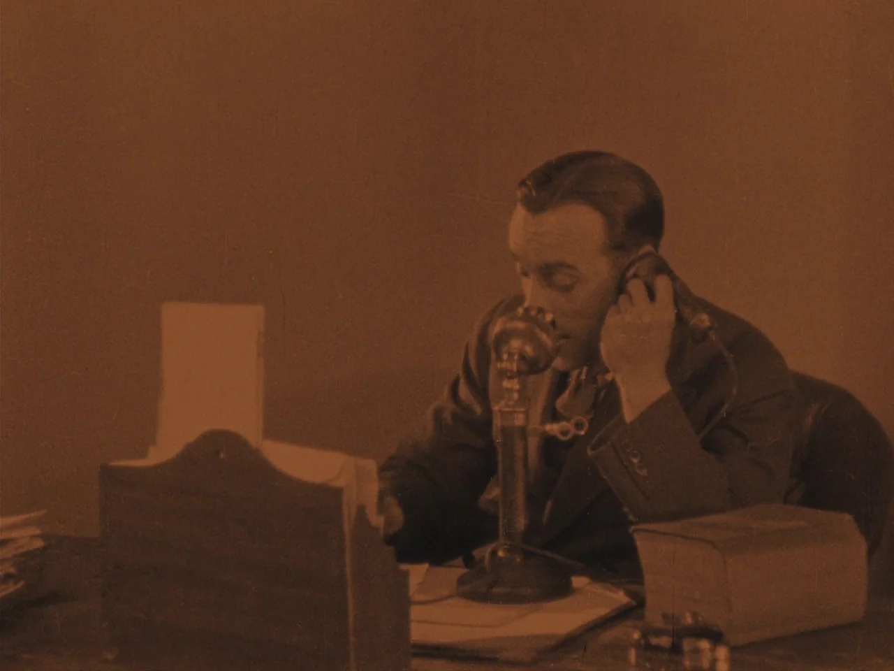 The Lodger (1927) movie still: medium — An interior space with a desk cluttered with period-specific business objects. A man in a suit is sitting at…