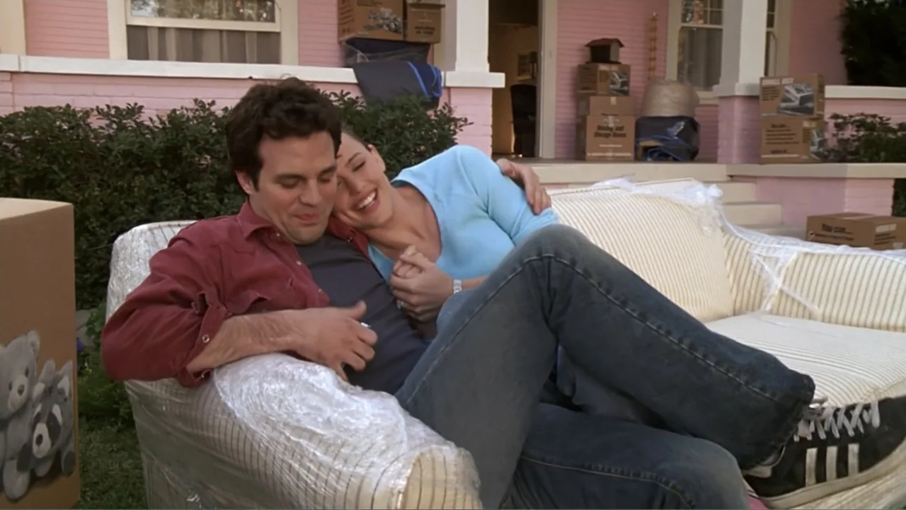 13 Going on 30 (2004) movie still: medium — A pink house exterior features a porch with cardboard boxes and a couch. A man and woman sit together on…
