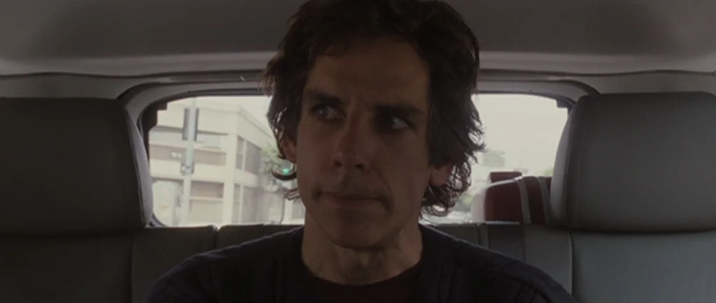 Greenberg (2010) movie still: closeup — A man sits inside the backseat of a car during the day. He looks forward as the vehicle drives through a…