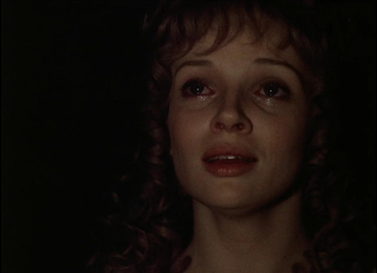 Beauty and the Beast (1979) movie still: closeup — The face of a young woman emerges from a dark, undefined space. She gazes upwards with a slight…
