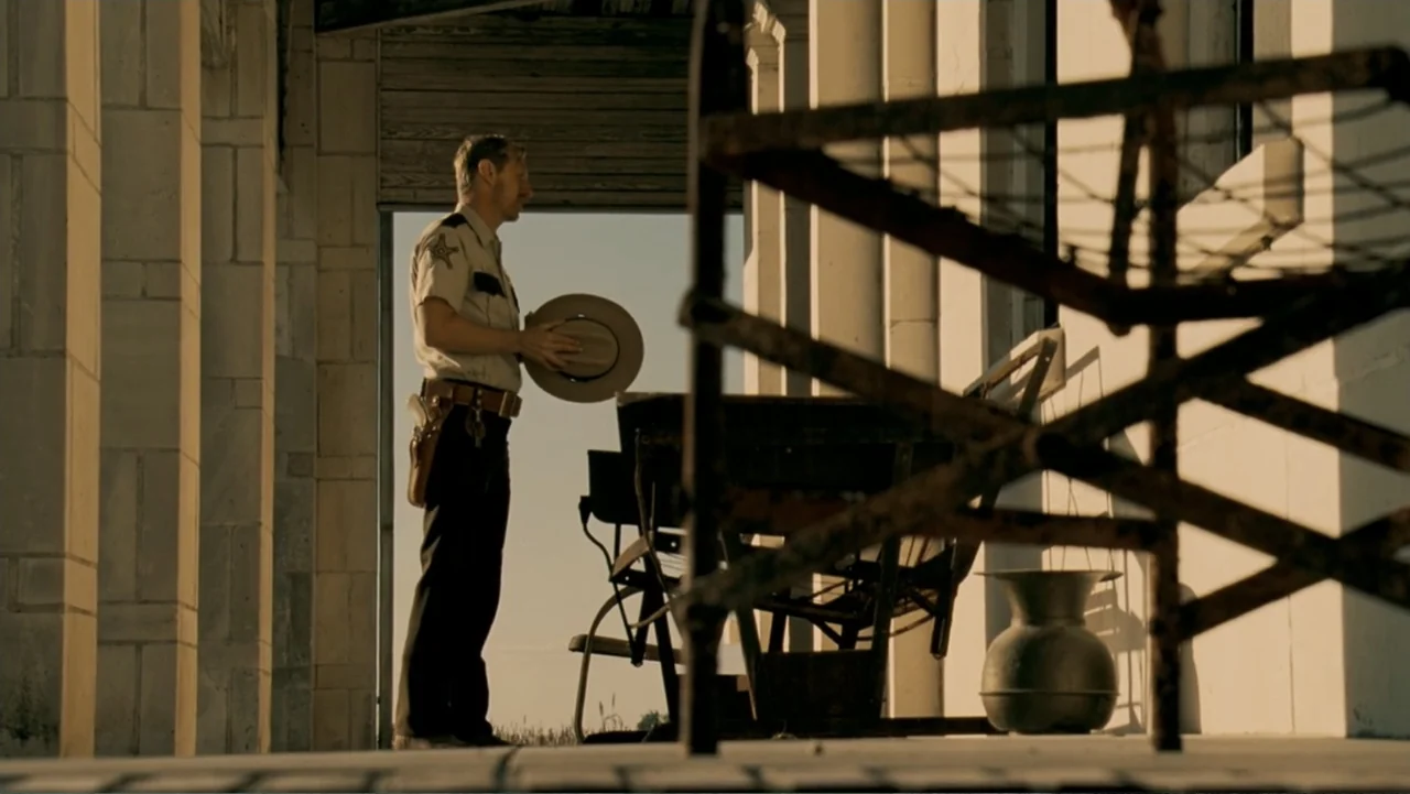 The Texas Chainsaw Massacre: The Beginning (2006) movie still: fullbody — A stone-columned porch with a rustic metal object sits in bright evening…