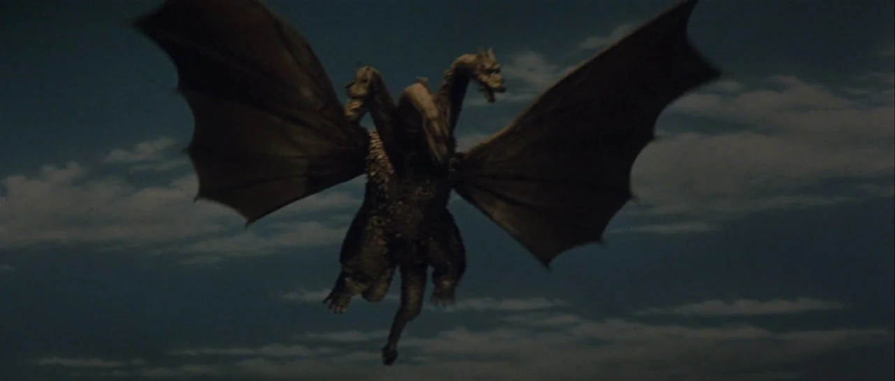 Godzilla Vs Gigan (1972) movie still: wide — A dark, overcast nighttime sky serves as the backdrop for a large creature. The three-headed monster…