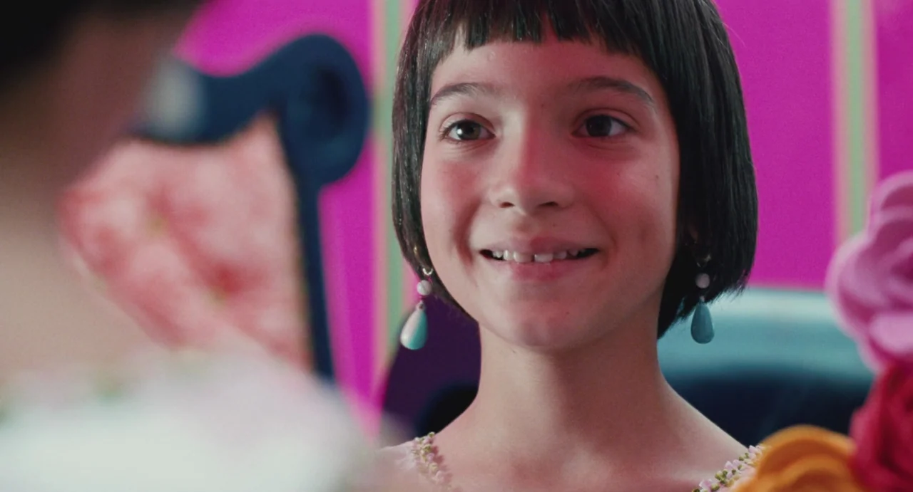 Ma Vie En Rose (1997) movie still: closeup — An interior space features a bright pink wall and vibrant colored decorative objects. A young girl with…