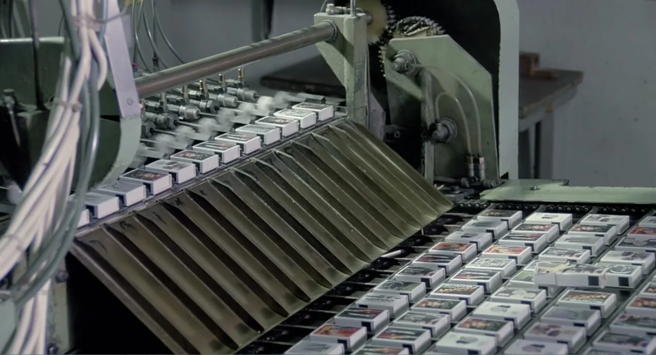 The Match Factory Girl (1990) movie still: medium — An automated assembly line processes matchboxes in a clean manufacturing environment. The…