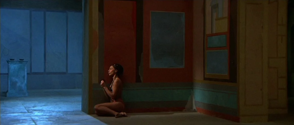 Fellini – Satyricon (1969) movie still: wide — A spacious room features walls painted in muted red, turquoise, and geometric abstract patterns. A…