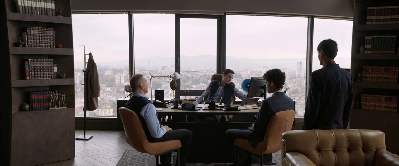 Marked Men: Rule + Shaw (2025) movie still: wide — A modern high-rise office features floor-to-ceiling windows overlooking a city skyline. Four men…