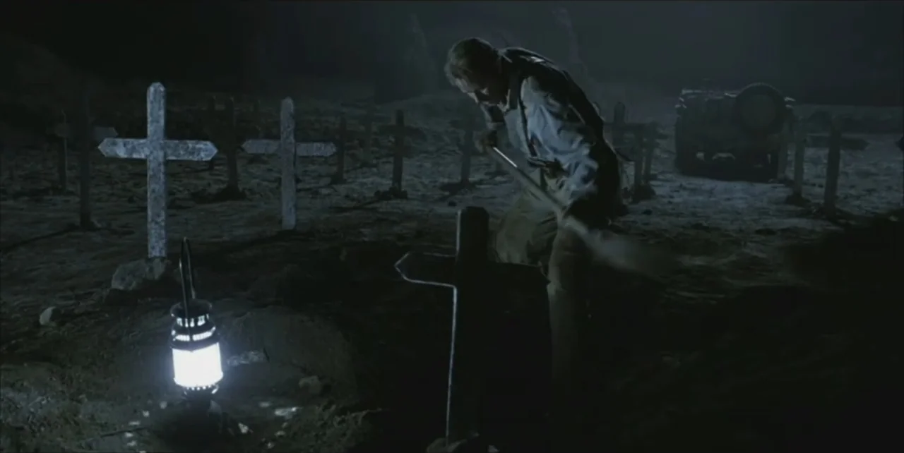 Exorcist: The Beginning (2004) movie still: medium — A dark graveyard filled with wooden crosses under a dim night sky. A man uses a shovel to dig a…