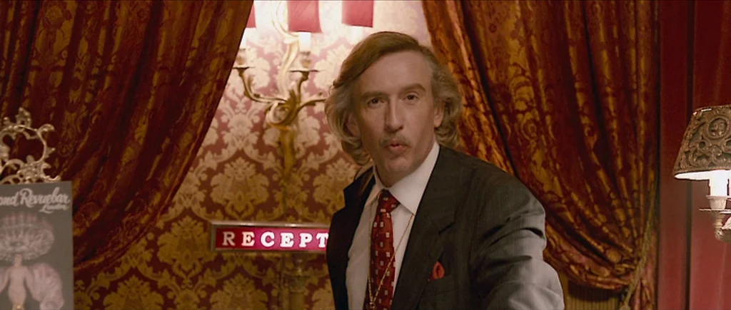 The Look of Love (2013) movie still: medium — A hotel reception area featuring ornate gold wallpaper and heavy dark red velvet curtains. A…