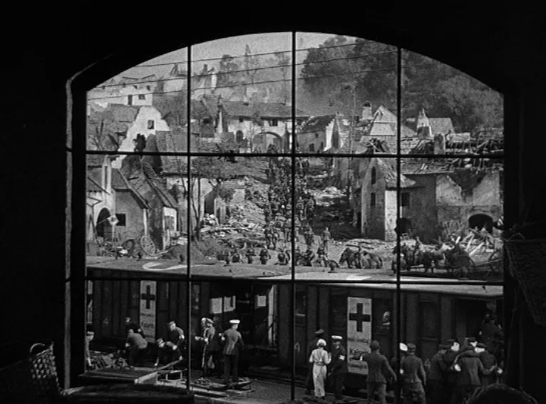 All Quiet on the Western Front (1930) movie still: establishing — A war-torn village with rubble-filled streets and damaged stone buildings visible…