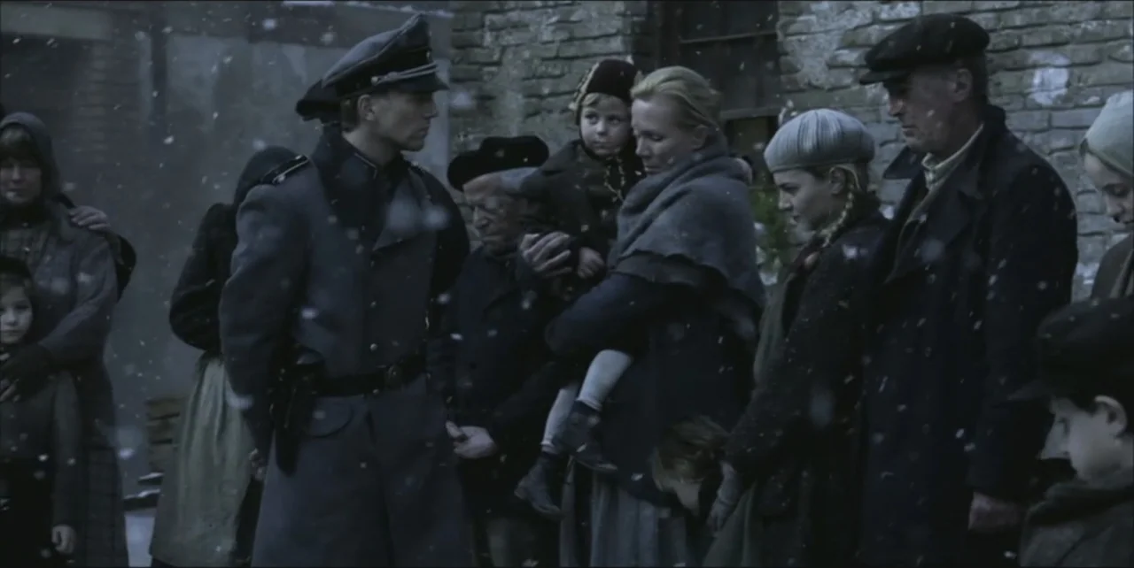 Exorcist: The Beginning (2004) movie still: medium — A snowy outdoor gathering features a German officer confronting a group of local civilians.…