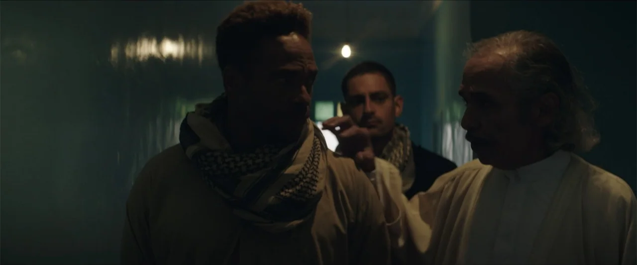 Redemption Day (2021) movie still: medium — A dimly lit narrow corridor with cool tones and a single faint light source. Three men in traditional…