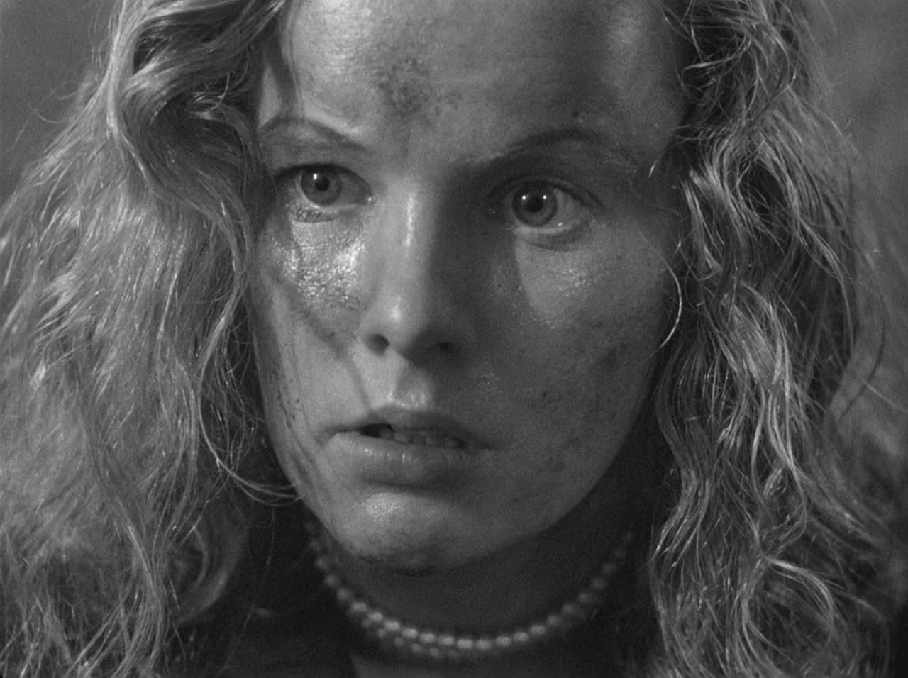 Gun Crazy (1950) movie still: closeup — A close-up of a woman in an indistinct, shadowed setting. The woman has a smudged face and curly hair while…