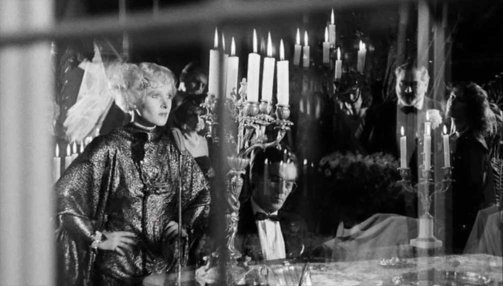 Veronika Voss (1982) movie still: medium — A formal dinner setting decorated with multiple ornate candelabras on a draped table. People in evening…